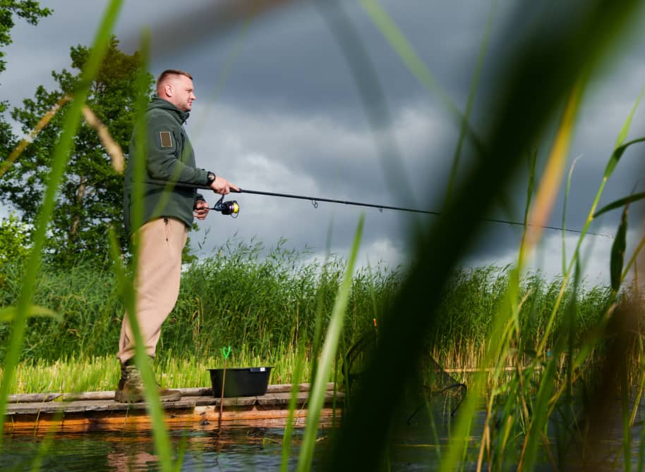 Angler am Ufer des Titisees zwischen Schilf unter bewölktem Himmel im Schwarzwald
