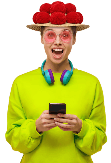 Eine Person, die ein leuchtend grünes Sweatshirt, eine rosafarbene Sonnenbrille, eine Mütze mit roten Bommeln und Kopfhörer trägt, lächelt und hält ein Smartphone in der Hand.