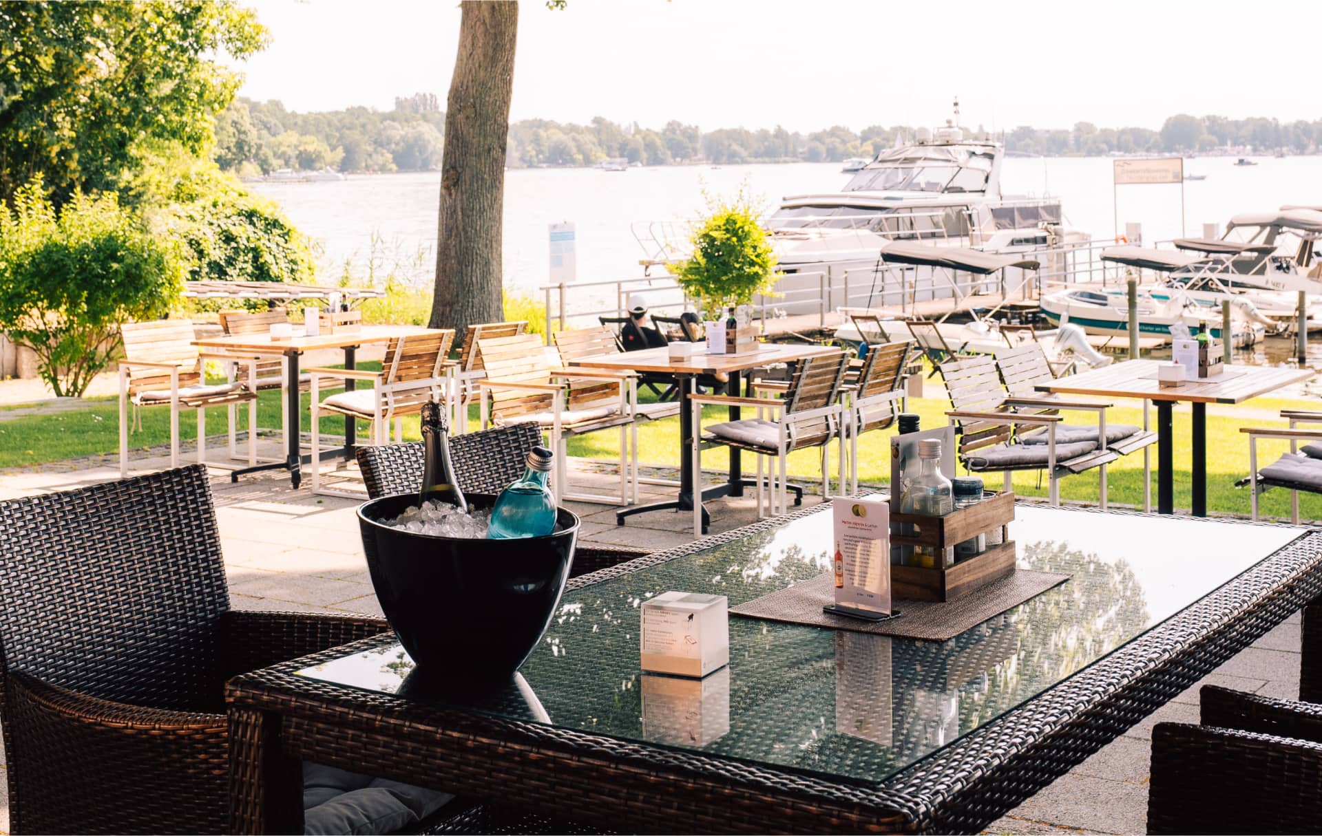 Seeterrasse mit Sektflasche im Kühler, edle Tischdekoration mit Seeblick
