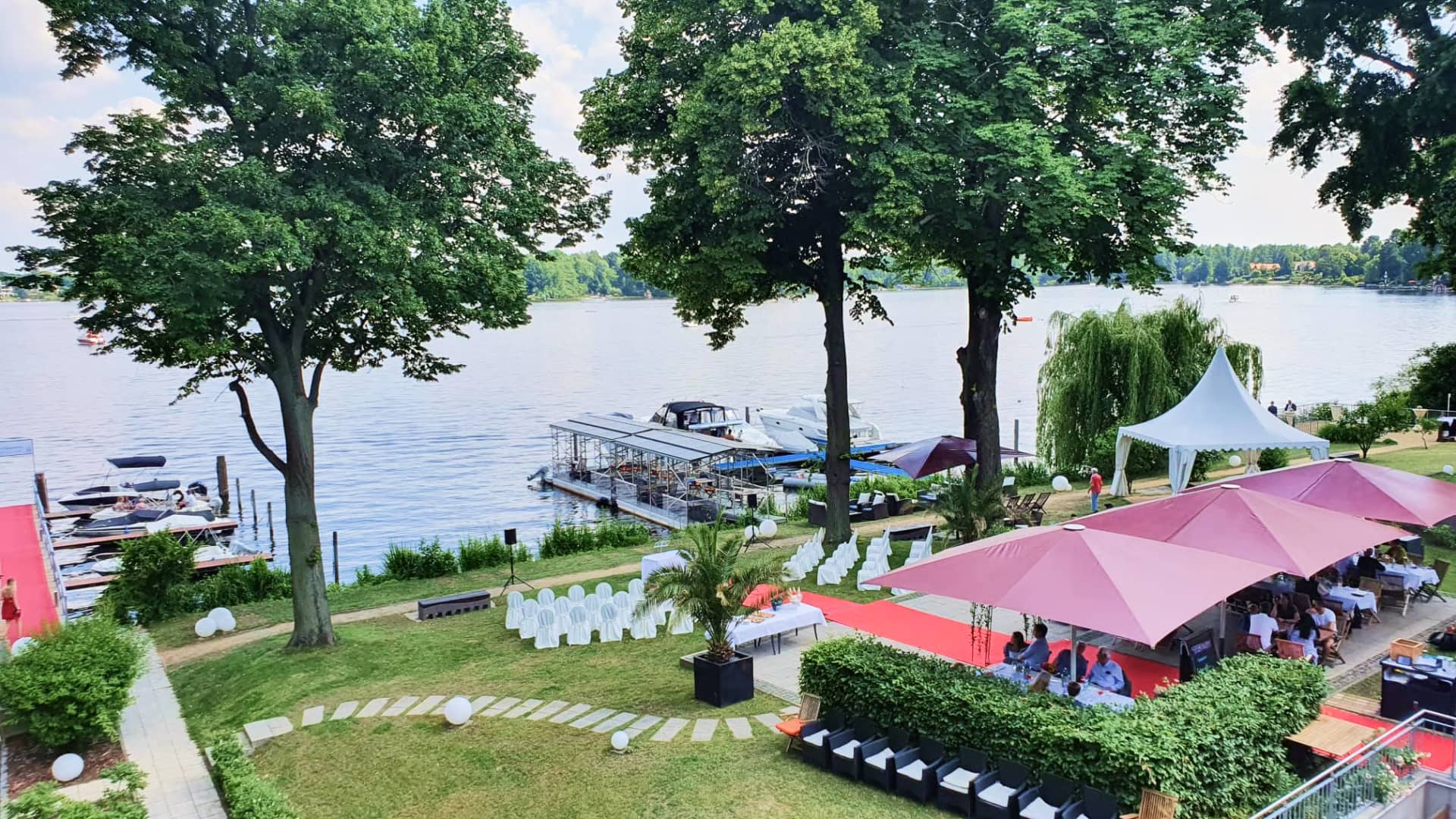 Luftaufnahme Seeufer-Event mit roten Zelten, weißen Stühlen und Bootssteg bei Sommerfest