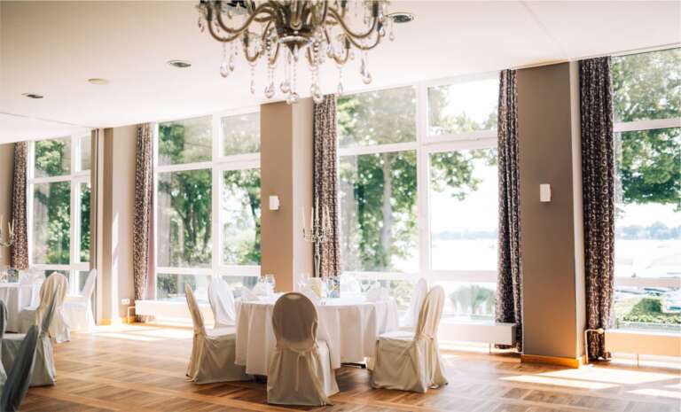 Heller Bankettsaal mit Kristalllüster, cremefarbenen Stuhlhussen und Seeblick
