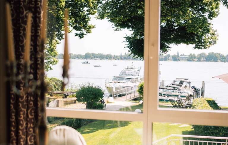 Fensterblick vom Restaurant auf Seeufer mit Booten und grüner Parklandschaft