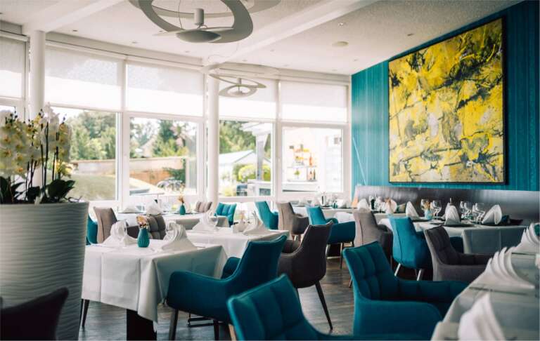 Modernes Restaurant mit türkisen Sesseln, abstraktem Kunstwerk und heller Atmosphäre