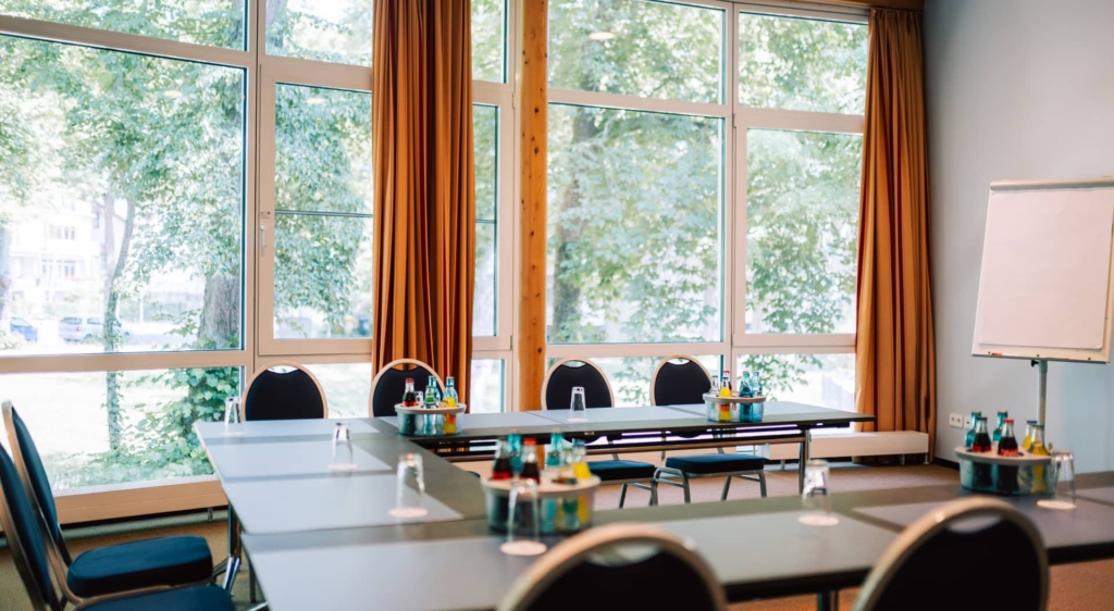Heller Konferenzraum mit großen Fenstern, schwarzen Stühlen und Flipchart