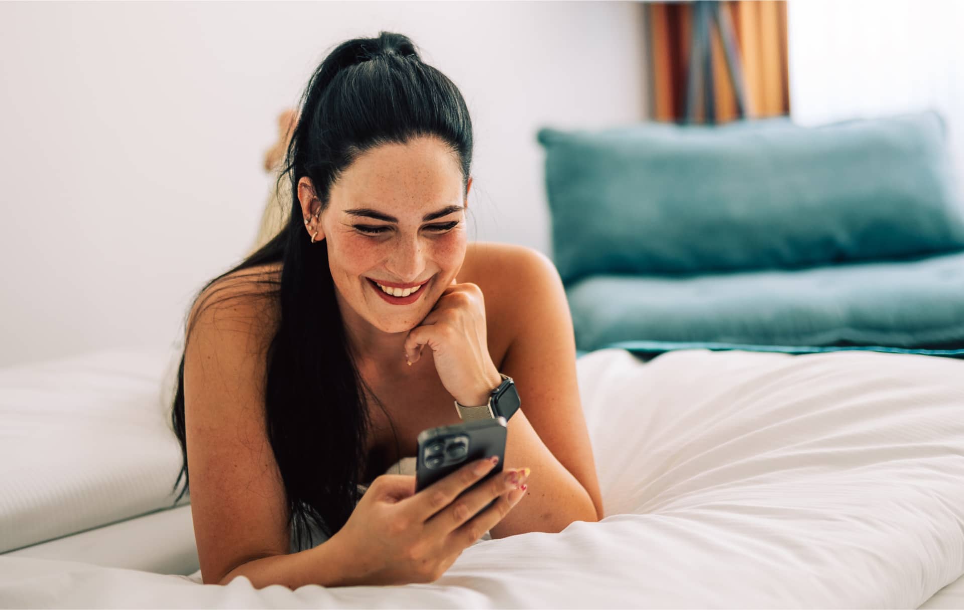 Lächelnde Frau mit Smartphone im Hotelbett, entspannte Atmosphäre