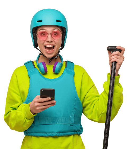 Eine Person in bunter Kleidung und mit Helm, die Kopfhörer trägt, ein Paddel in der Hand hält und lächelnd auf ihr Smartphone schaut.