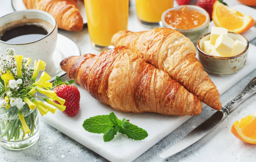 Frische süße Croissants mit Butter und Orangenmarmelade zum Frühstück.