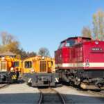 Historische Diesellokomotiven und eine rote Lok der Harzer Schmalspurbahnen auf Abstellgleisen im Bahnhofsumfeld