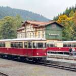 Zwei historische Triebwagen der Harzer Schmalspurbahnen stehen am Bahnhof vor bewaldeter Harz-Kulisse