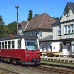 Roter Triebwagen der Harzer Schmalspurbahnen hält am Bahnhof Elend vor historischen Fachwerkhäusern