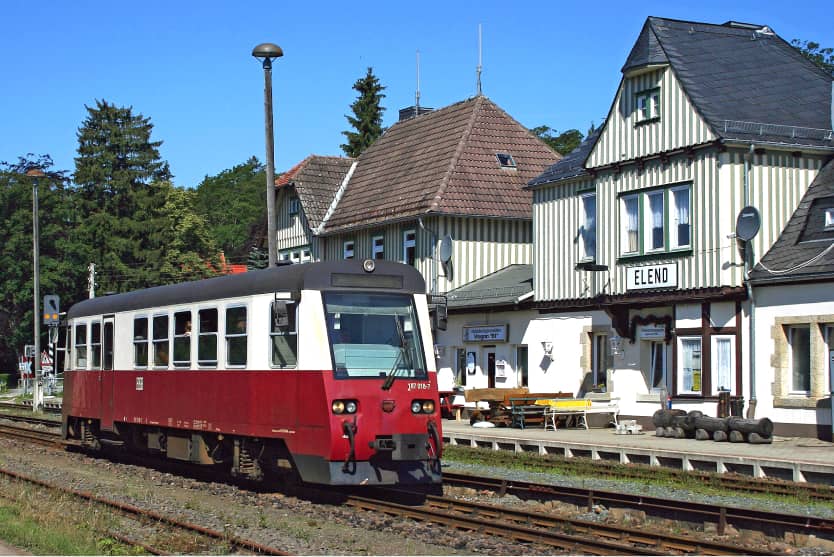 Roter Triebwagen der Harzer Schmalspurbahnen hält am Bahnhof Elend vor historischen Fachwerkhäusern