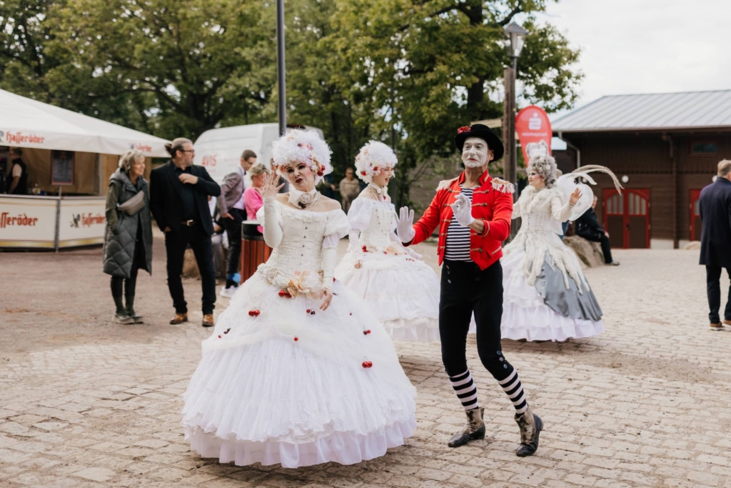 Barockkostümierte Darsteller und ein Pantomime begrüßen Besucher auf dem gepflasterten Theaterplatz.