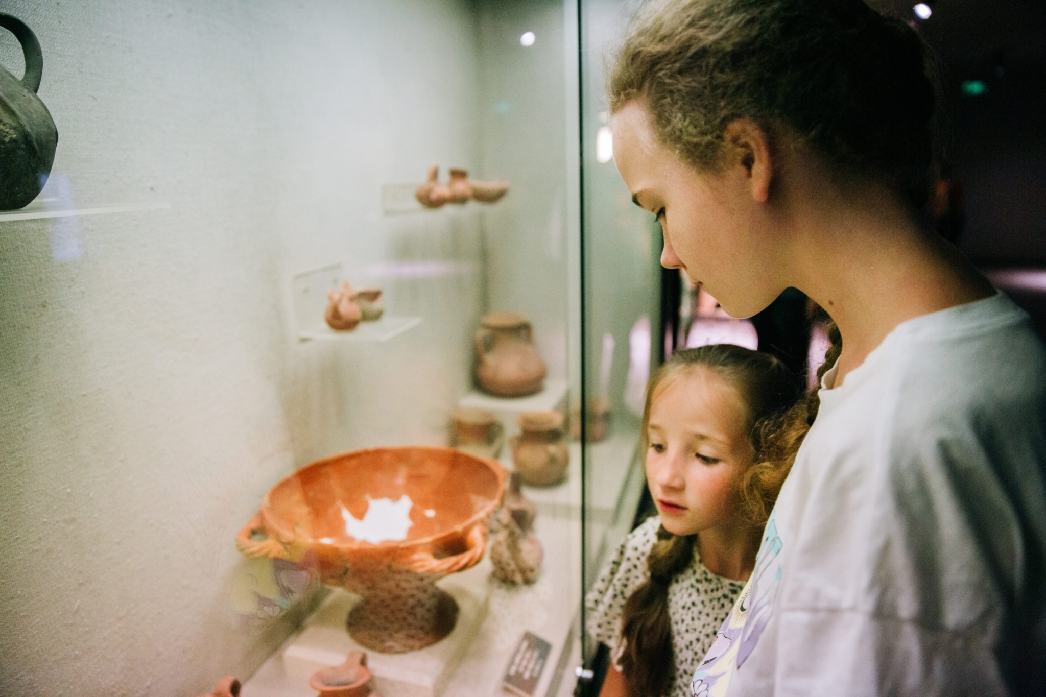 Zwei junge Mädchen betrachten in einer Museumsausstellung eine Ausstellung antiker Töpferwaren und Artefakte hinter Glas.