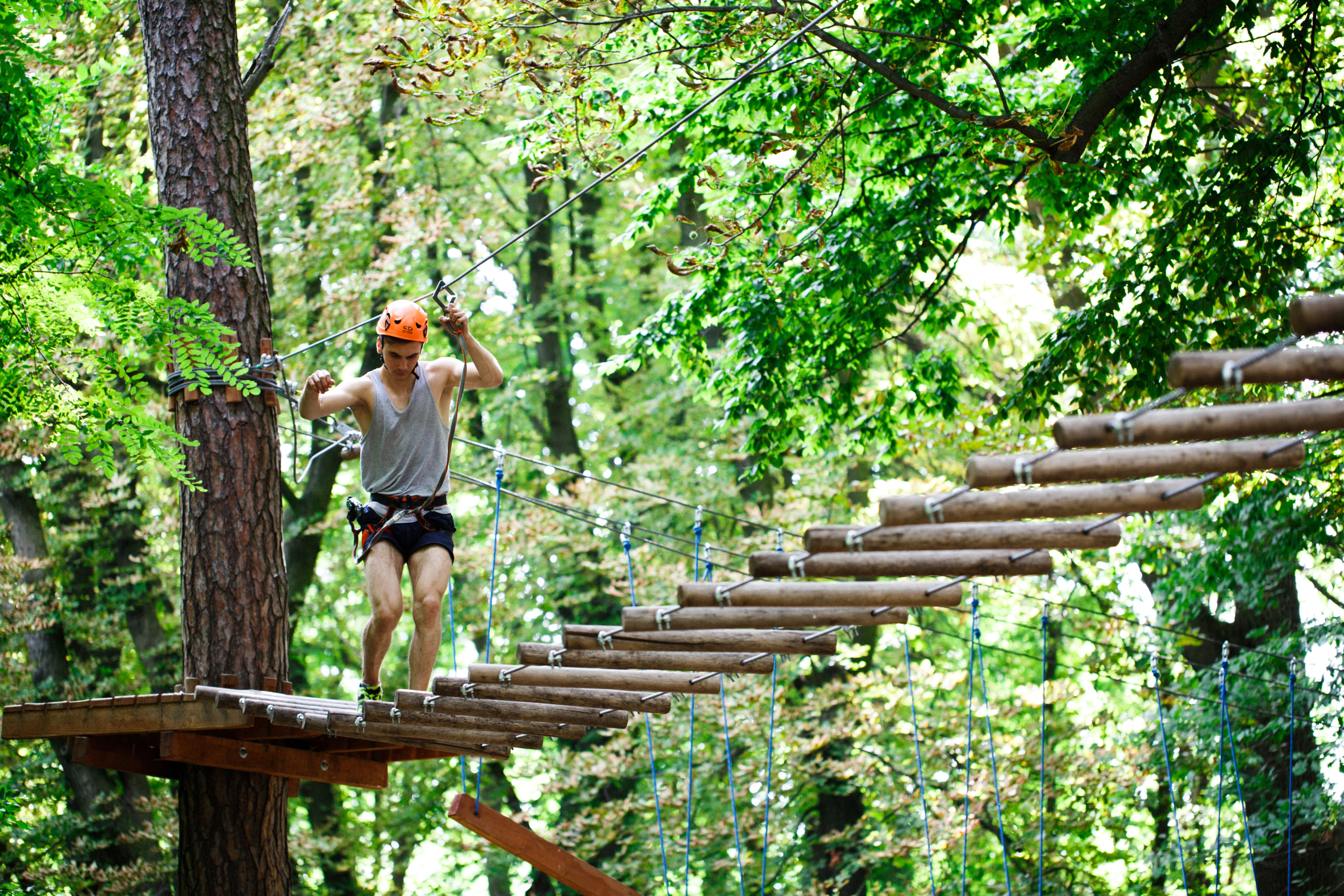 Eine Person überquert mit einer Sicherheitsausrüstung eine Seilbrücke aus Holzbohlen im Kletterwald Thale im Wald.