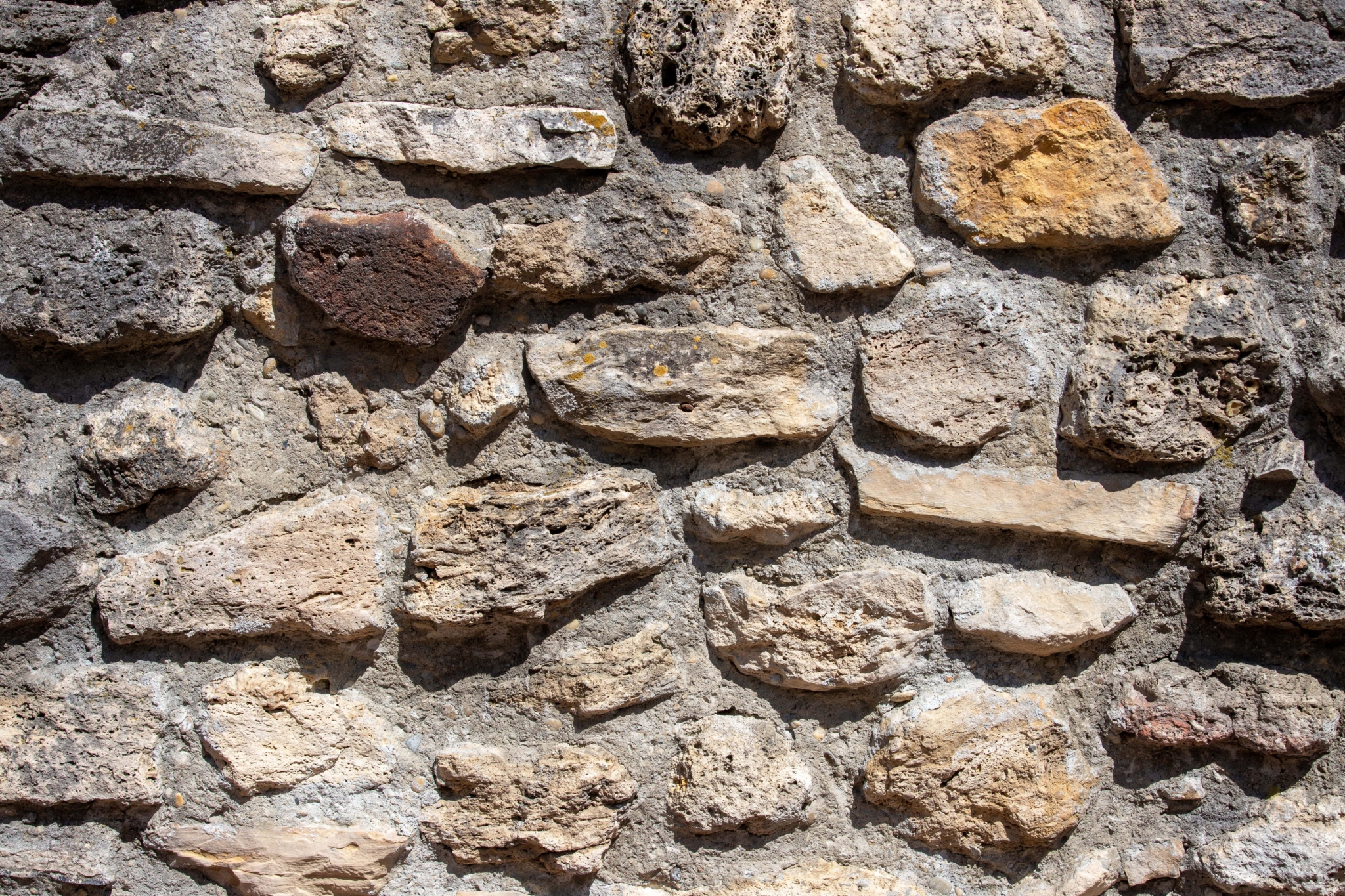 Nahaufnahme einer alten, unebenen Steinmauer aus Steinen unterschiedlicher Größe und Farbe, die durch groben Zement zusammengehalten werden.