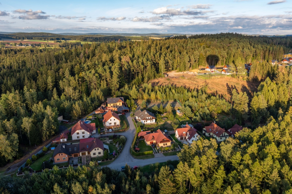 Luftaufnahme der Ferienhäuser vom H24 Hotel in Thale, umgeben von Wald, mit dem Schatten eines Heißluftballons, der auf den Bäumen und dem Boden sichtbar ist.