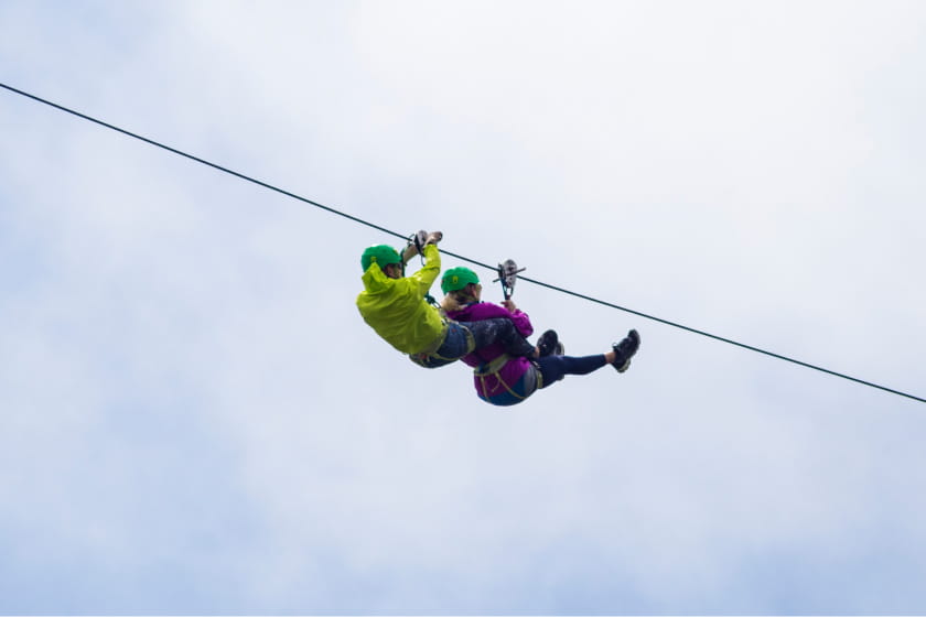 Zwei Personen mit Helm und Gurtzeug seilen sich Seite an Seite gegen den wolkenverhangenen Himmel ab und erleben den Nervenkitzel beim Harzdrenalin.