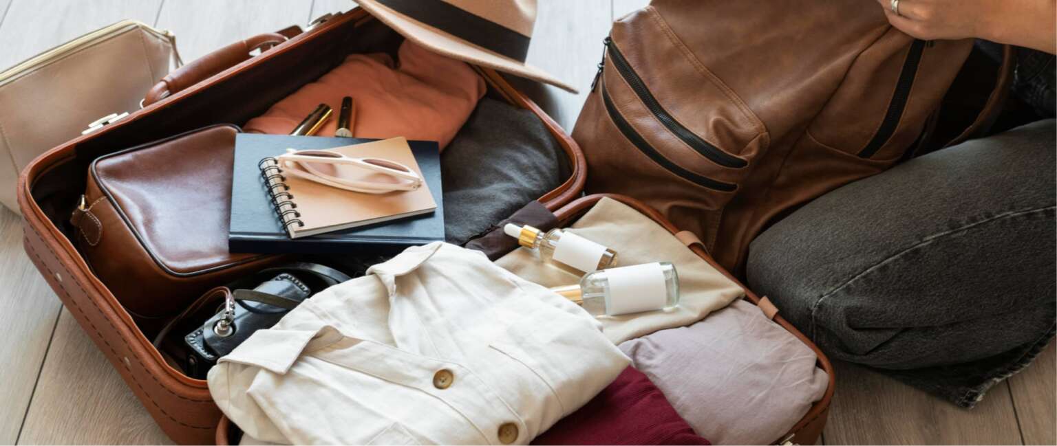 Koffer offen, Kleidung und Accessoires wie Hut, Notizbuch und Sonnenbrille sind sichtbar