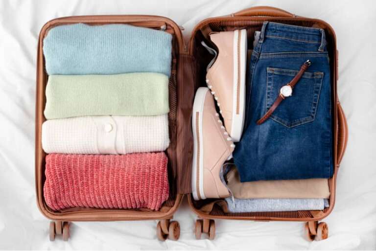 Koffer ordentlich gepackt, Pullover und Jeans, Schuhe und Uhr sauber sortiert nebeneinander