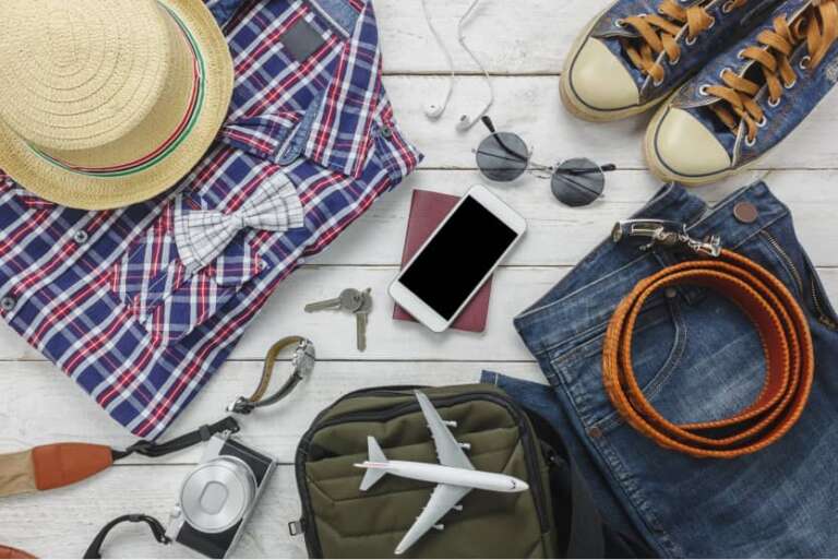 Outfit für die Reise: Kleidung und Accessoires wie Hut, Kamera, Schlüssel und Modellflugzeug