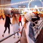 Winterliche Eislaufbahn mit Lichterketten, Menschen und beleuchtetem Riesenrad im Hintergrund