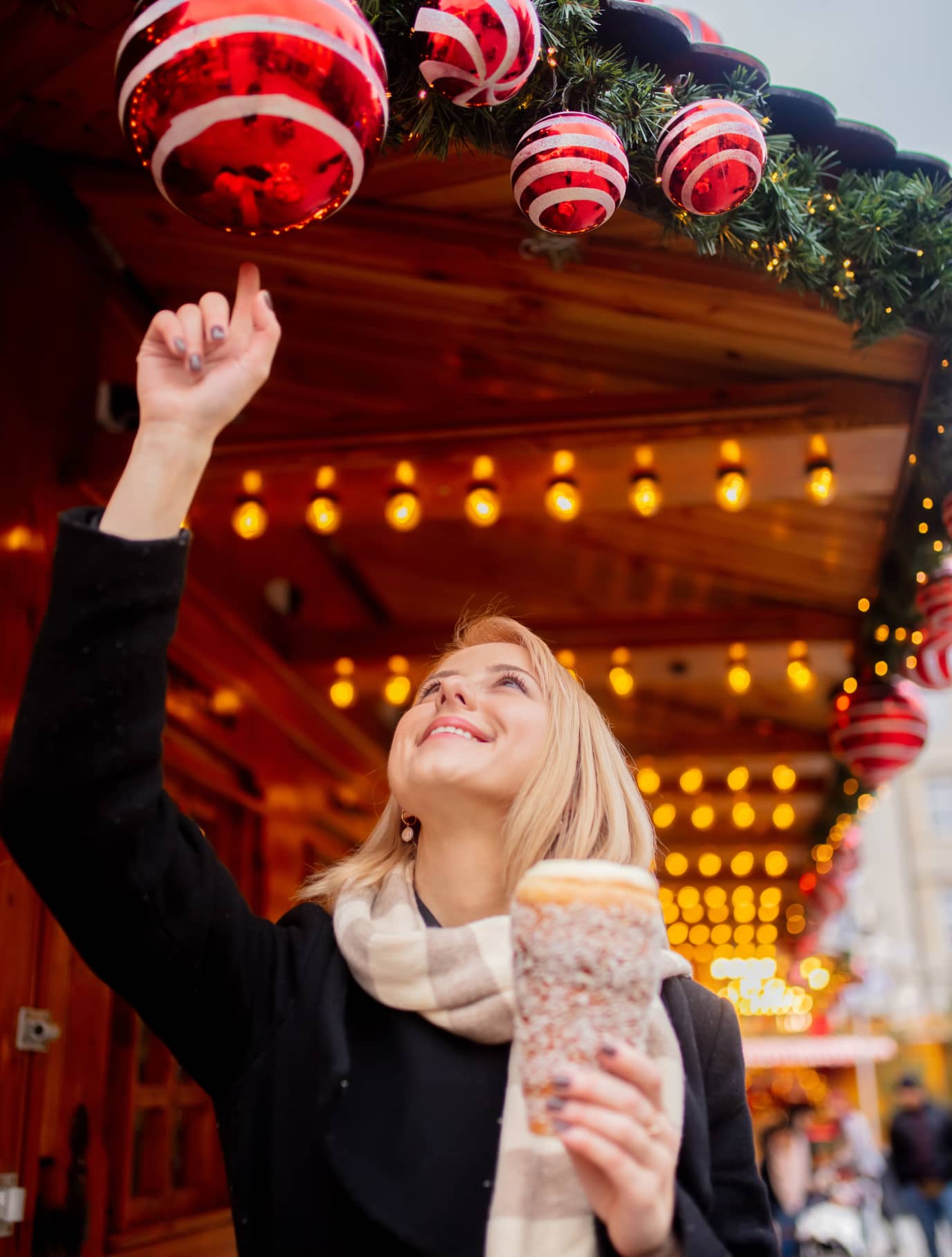Frau auf dem Weihnachtsmarkt, greift nach roten Kugeln und hält süßes Gebäck in der Hand