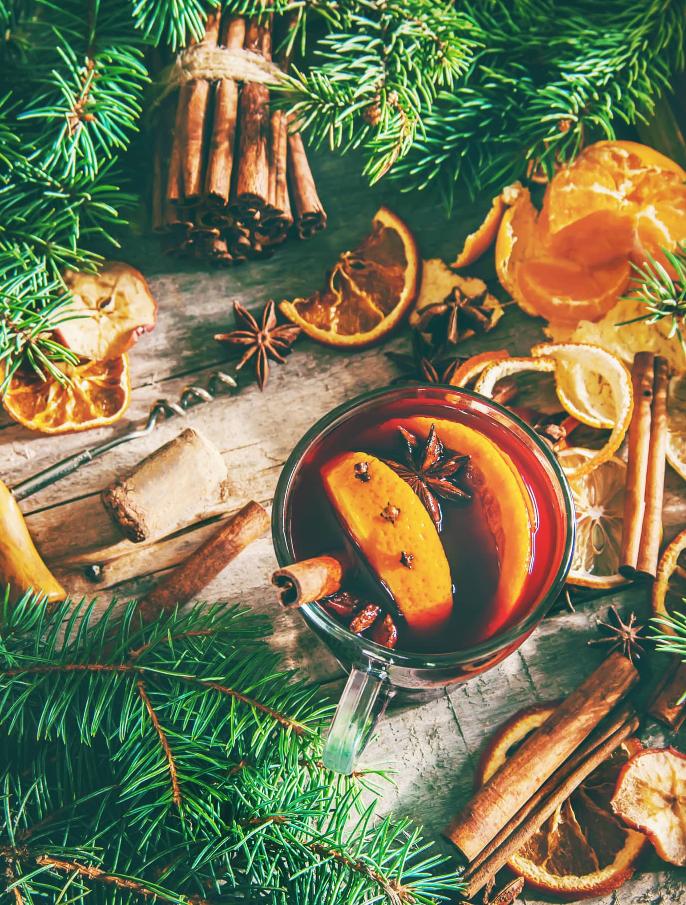 Tasse Glühwein mit Gewürzen, Orangenscheiben und Tannenzweigen auf einem Holztisch