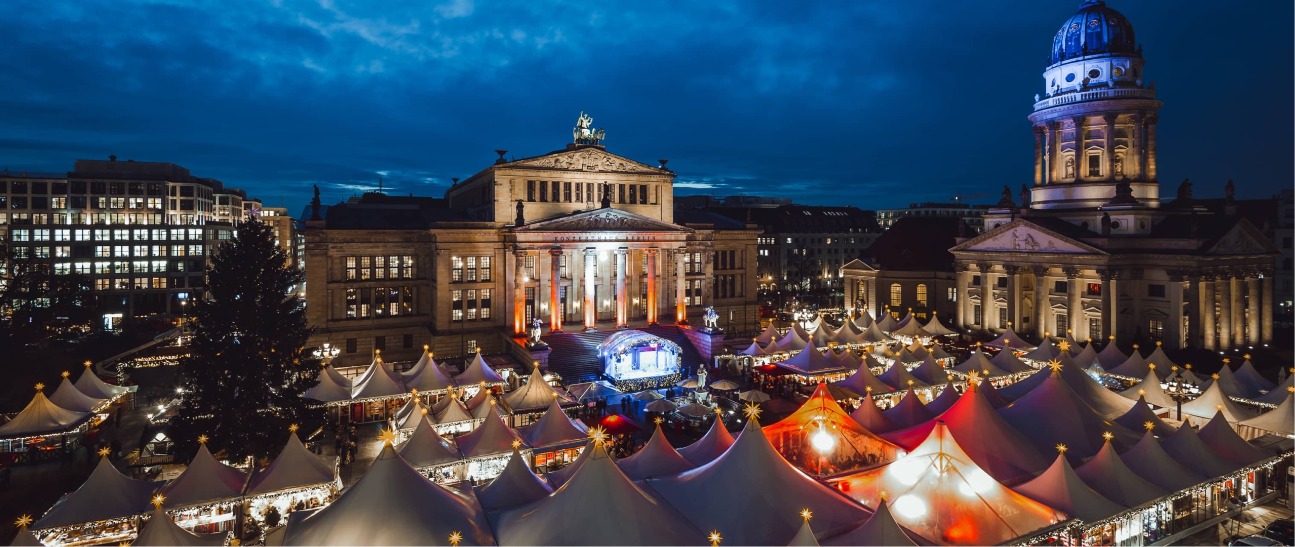 Weihnachtsmarkt am Gendarmenmarkt: Festliche Zelte vor beleuchteten historischen Gebäuden.