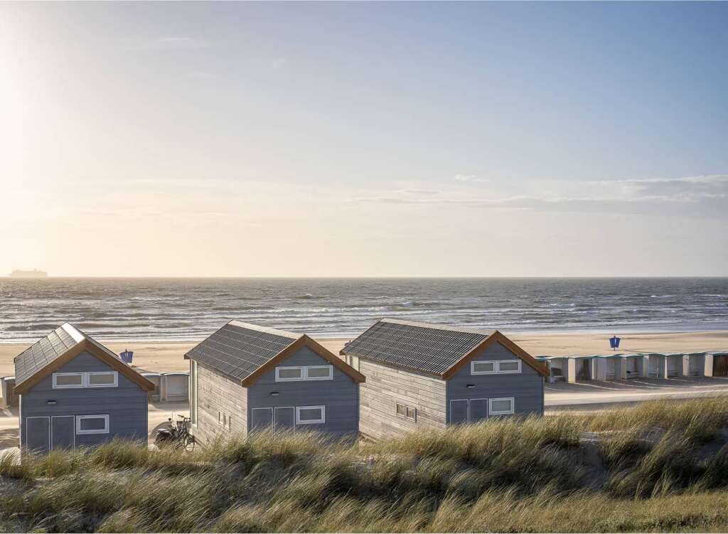 Drei kleine blaue Strandhäuser mit Blick auf den Sandstrand und das Meer.