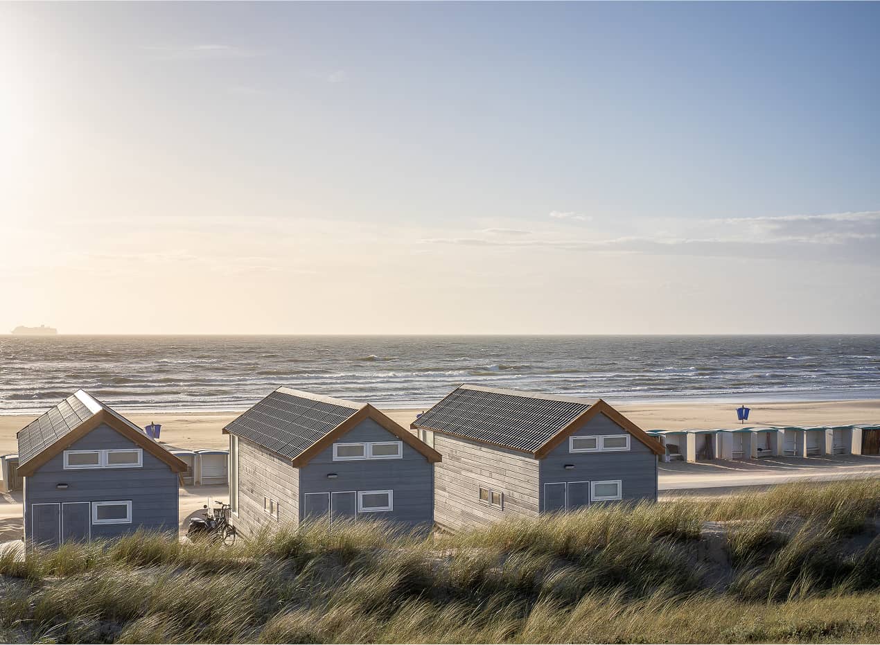 Drei kleine blaue Strandhäuser mit Blick auf den Sandstrand und das Meer.