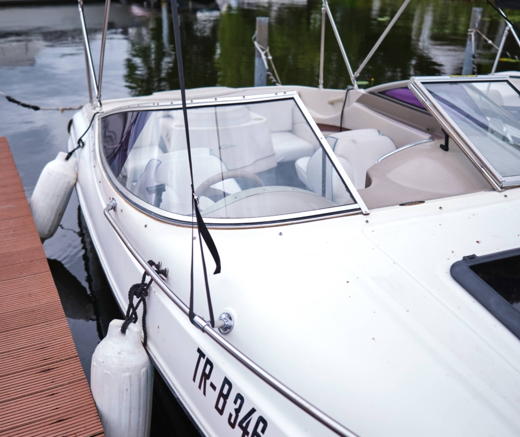 Ein weißes Motorboot mit dem Kennzeichen TR-B346, buchbar über den Bootsverleih Berlin, liegt an einer mit Sicherungsbojen und Festmacherleinen ausgestatteten Anlegestelle auf einem ruhigen Gewässer in der Nähe des H24 DämeritzSeeHotels.