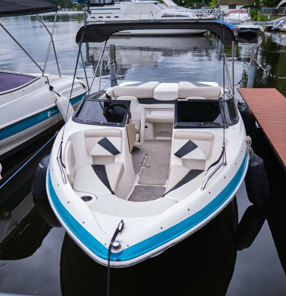 Ein blau-weißes Schnellboot, das in der Marina des H24 DämeritzSeehotels angedockt ist, mit Sitzgelegenheiten vorne und hinten und einem Dach darüber – perfekt für Ihr nächstes Bootsverleih-Berlin-Abenteuer.