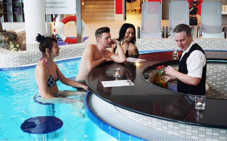 Badegäste genießen Getränke an einer Swim-up-Bar im Wasser, bedient von einem Barkeeper in Uniform.