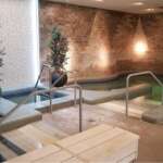 Innenbereich eines Spa-Pools mit warmen Licht, Pflanzen in großen Töpfen und einem Becken mit Handläufen zum Entspannen.
