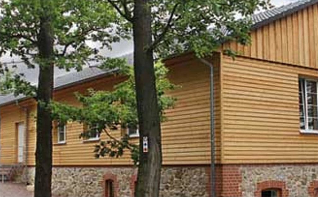 Längliches Holzhaus im Grünen, rote Backsteinfundamente, umgeben von Bäumen