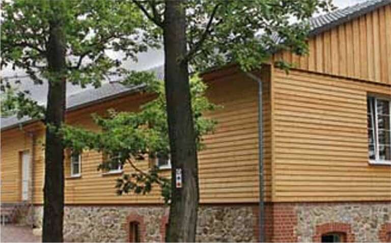 Längliches Holzhaus im Grünen, rote Backsteinfundamente, umgeben von Bäumen