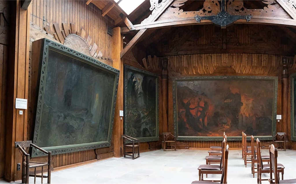Großer, holzgetäfelter Saal mit riesigen düsteren Gemälden und Reihen von Holzstühlen